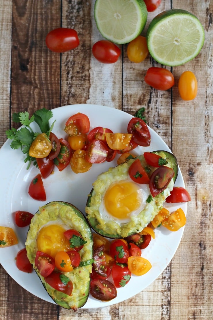 Mexican grilled avocado eggs topped with cherry tomato salsa and cilantro on a white plate with limes