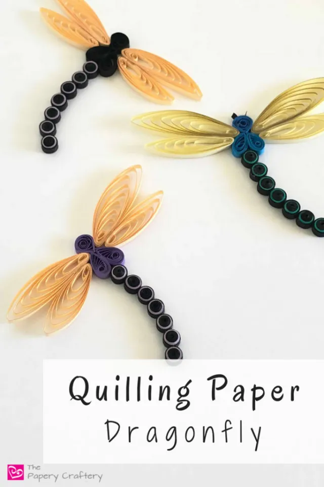Two quilled paper dragonflies, one black bodied and one purple, with peach teardrop wings beside a quilling comb