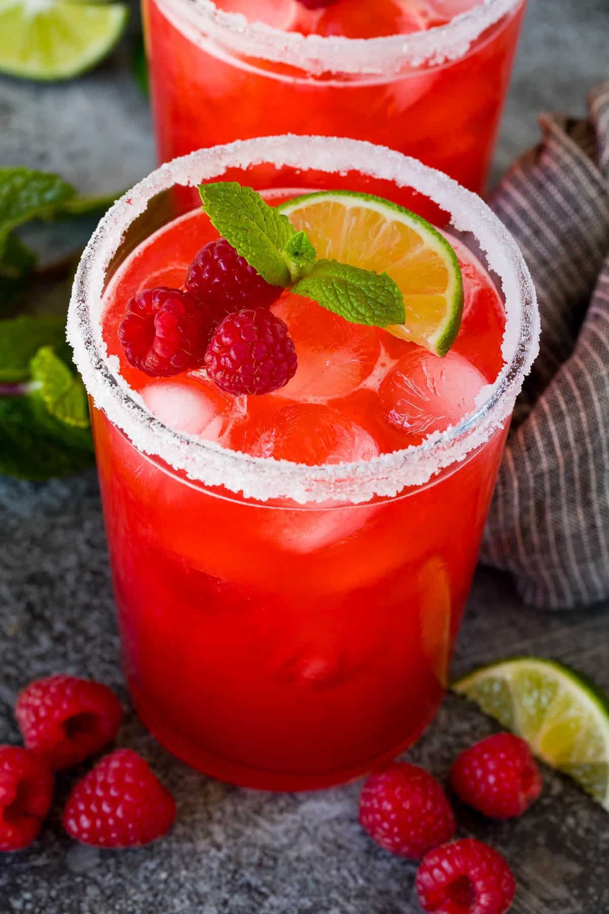 Ruby red raspberry margarita on ice in a salt-rimmed glass with raspberries, mint and a lime wedge