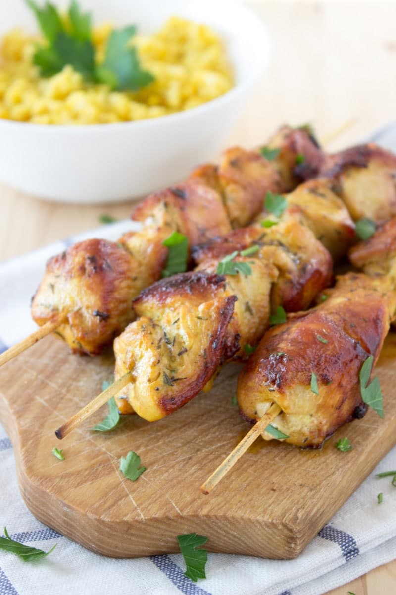 Golden grilled soy marinated chicken skewers on a wooden board with a bowl of yellow bulgur behind