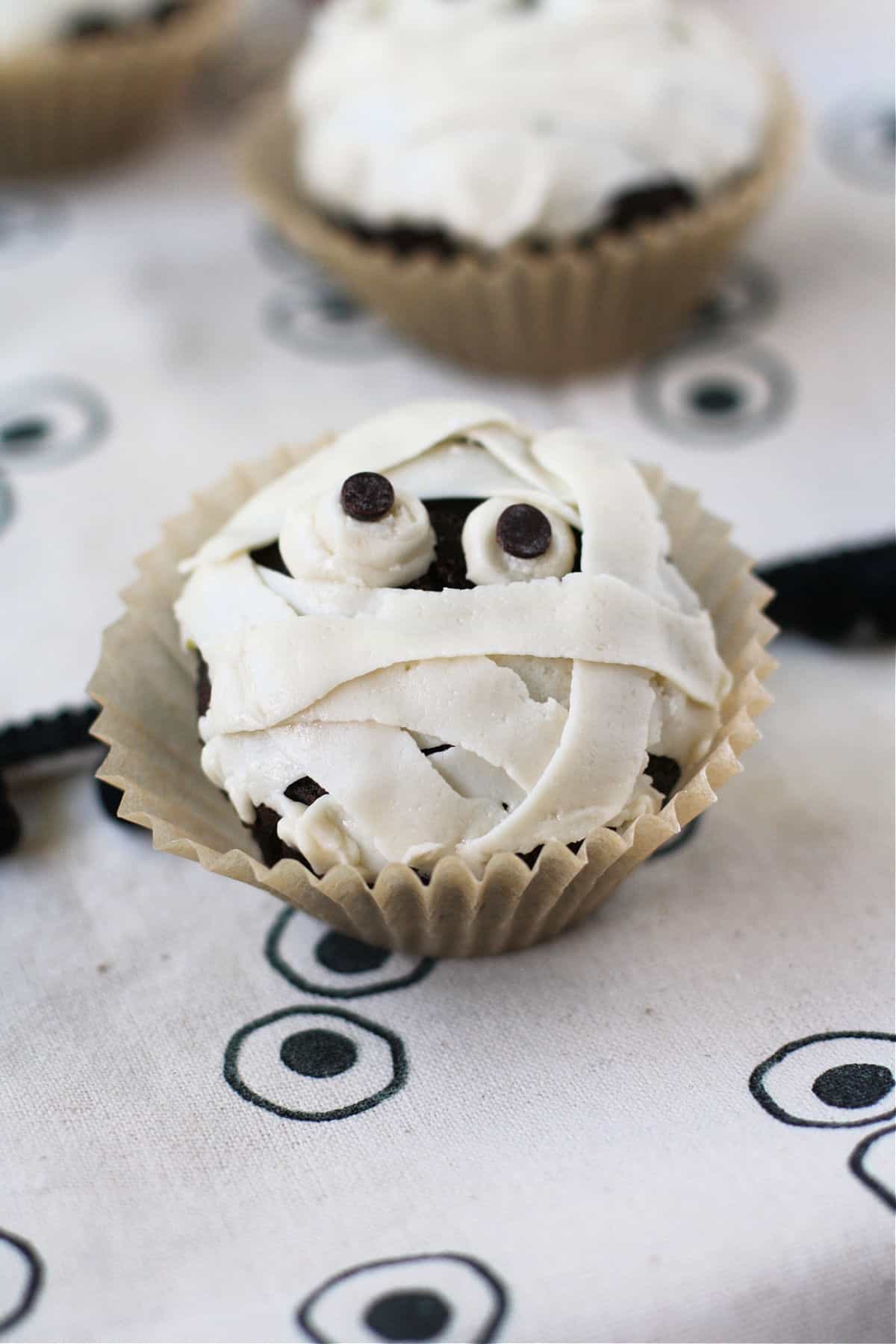 Chocolate cupcake wrapped in white frosting mummy bandages with two candy eyes peeking out