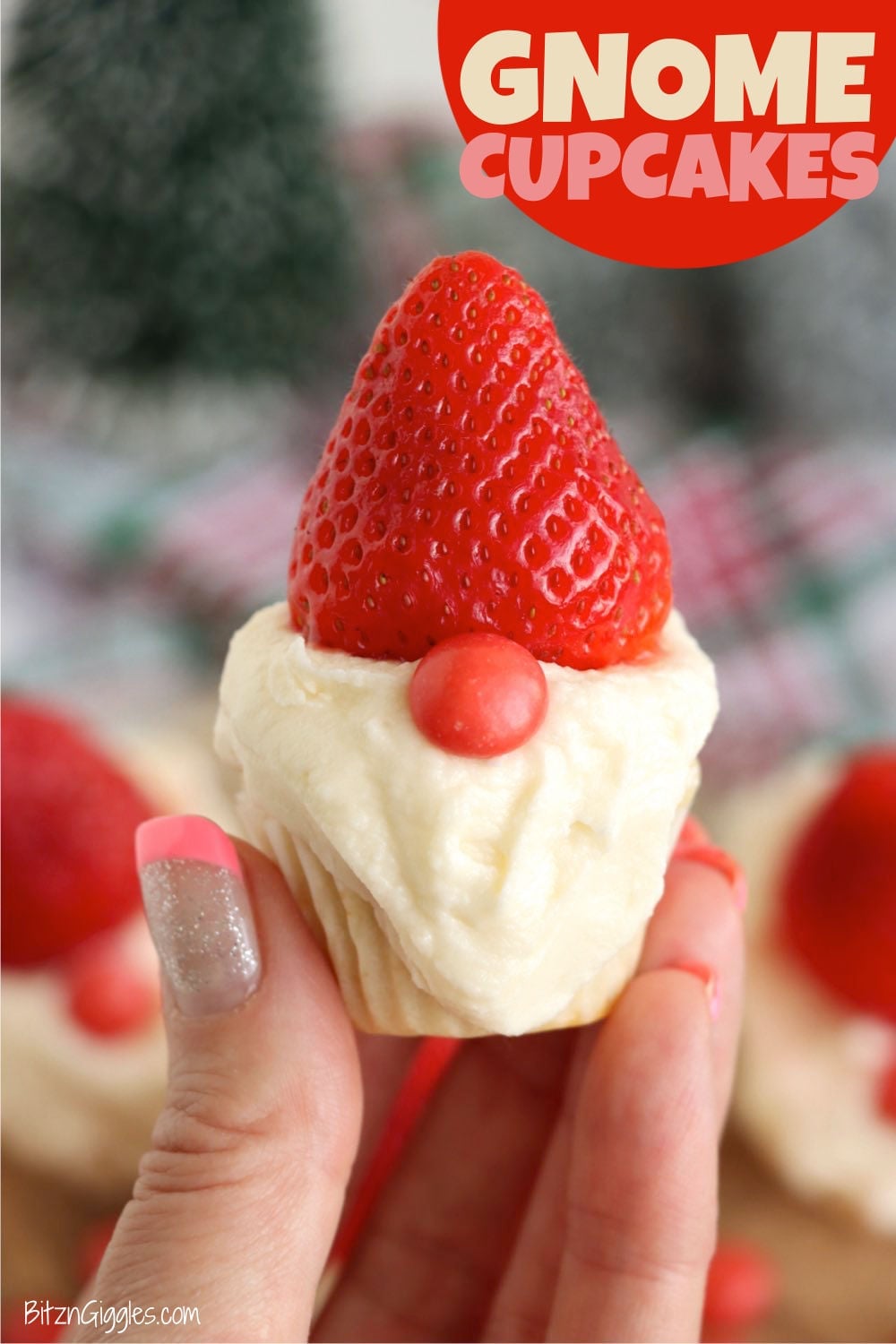 Cupcake with a fluffy white frosting beard, a whole strawberry hat and a round red candy nose, held in a hand