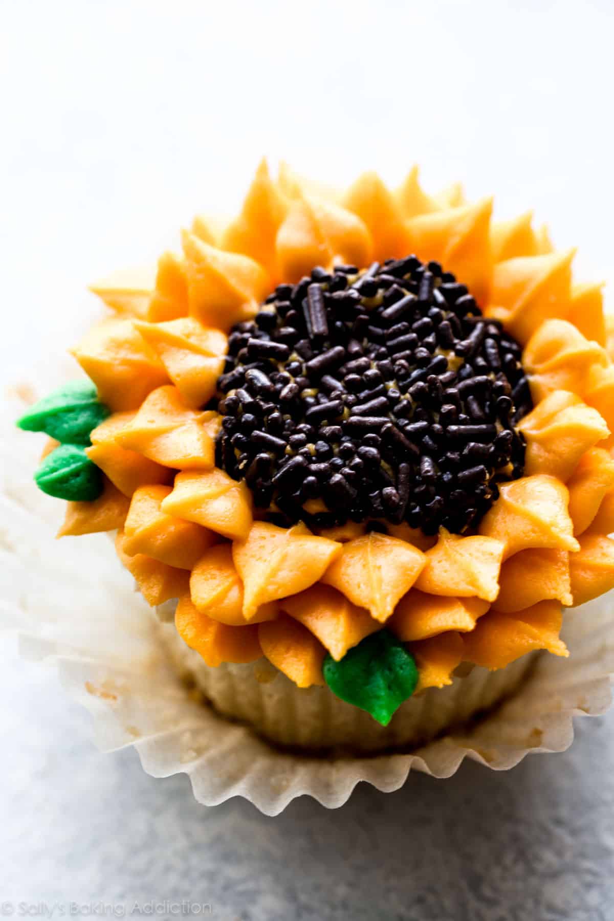 Cupcake piped with orange and yellow pointed buttercream petals around a center of chocolate sprinkles