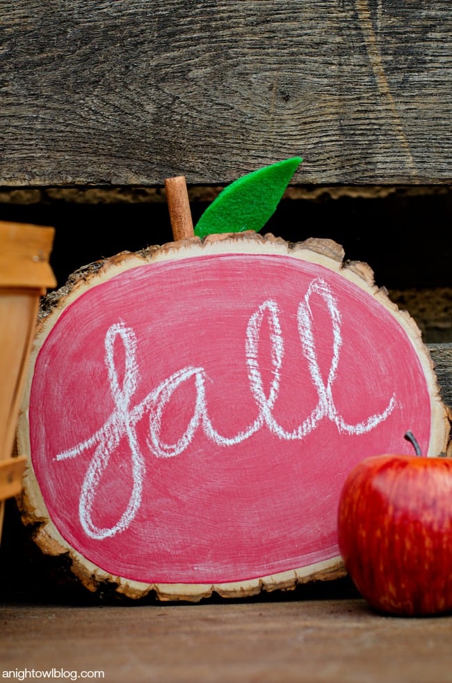 Round wood slice painted with red chalkboard paint like an apple with a felt leaf, lettered fall in chalk beside red apples