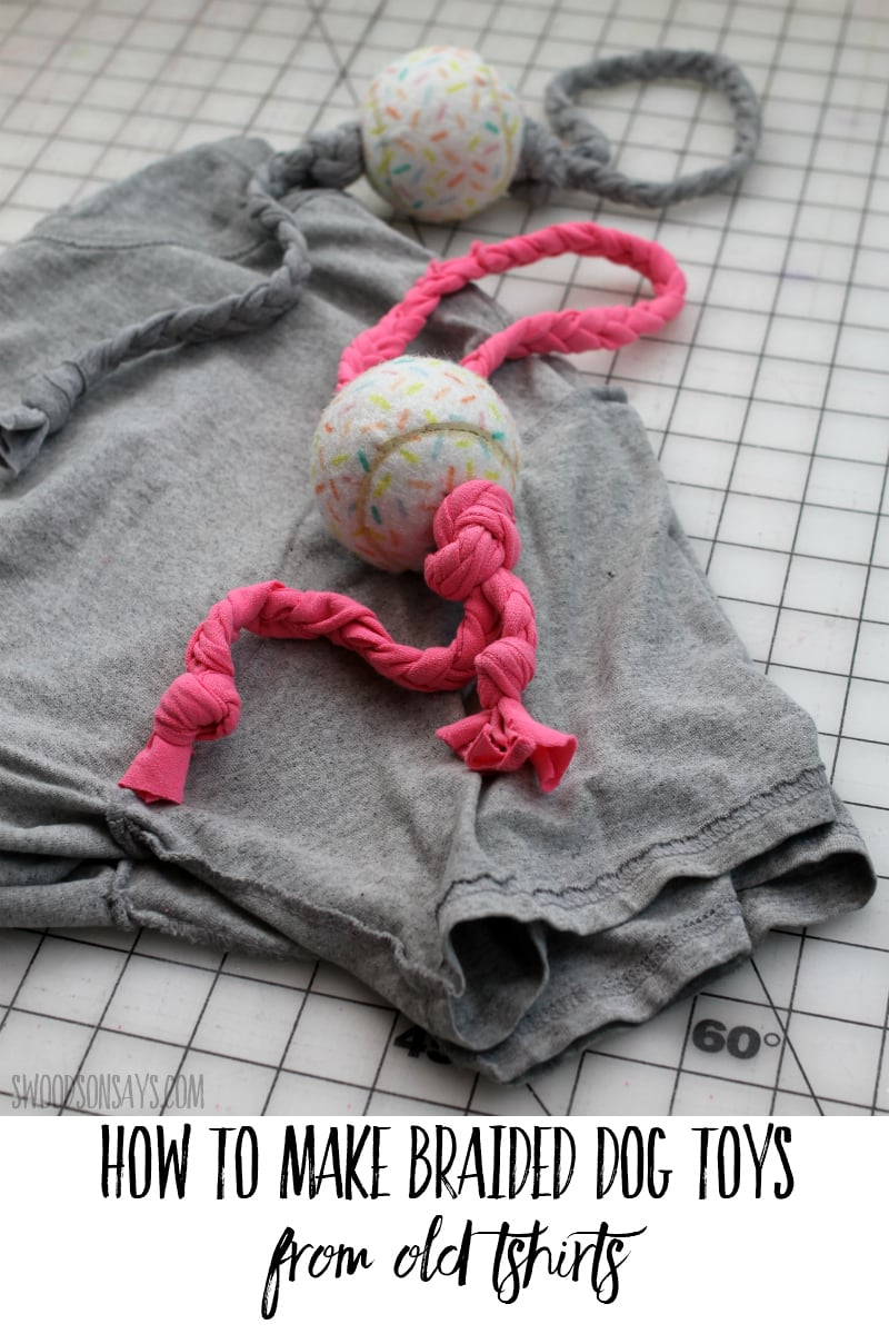 Two braided t-shirt dog toys in pink and gray with tennis balls threaded on the braids, lying on a gray shirt