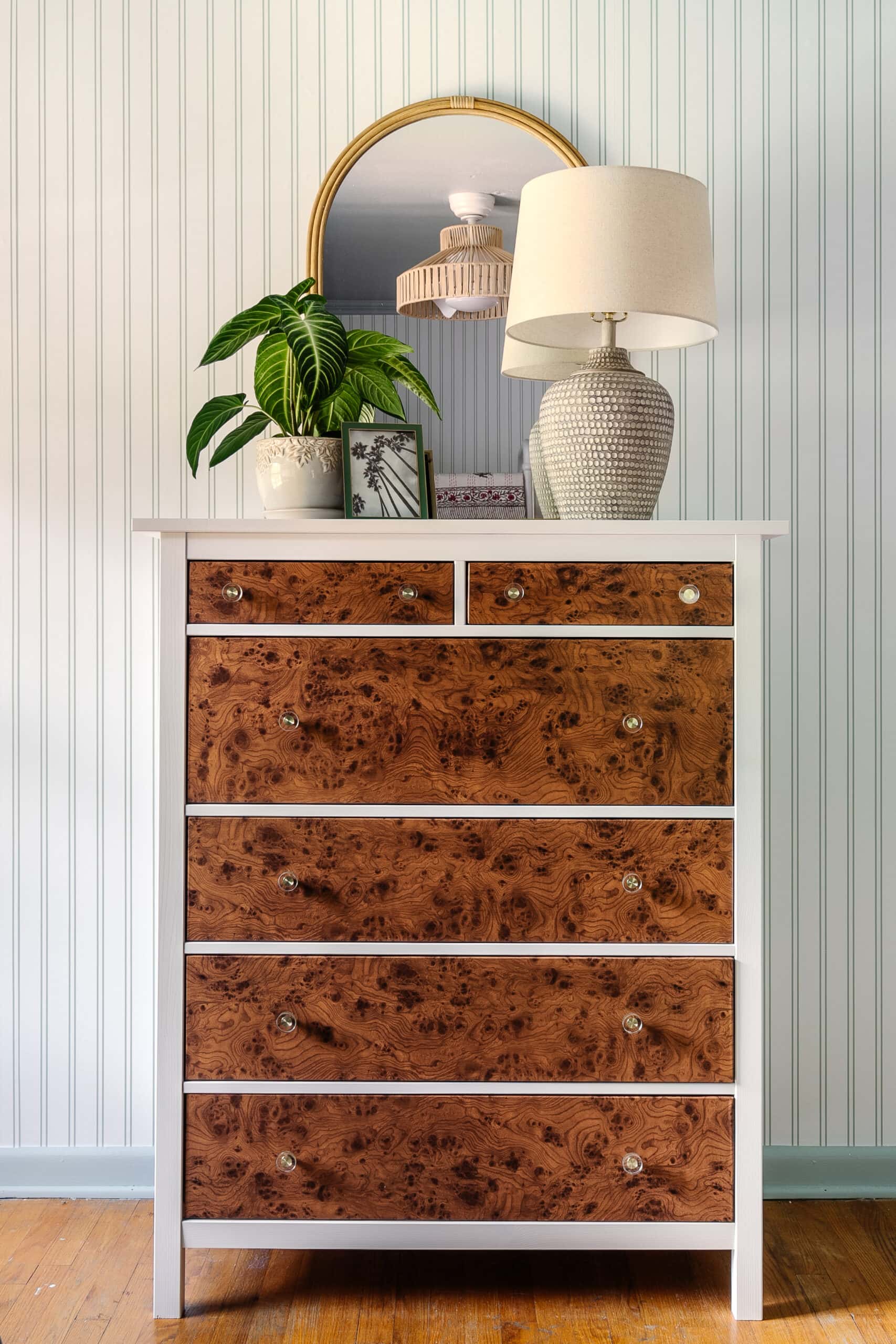 IKEA Hemnes chest with burl wood contact paper drawer fronts, glass knobs, white frame and a lamp and plant on top