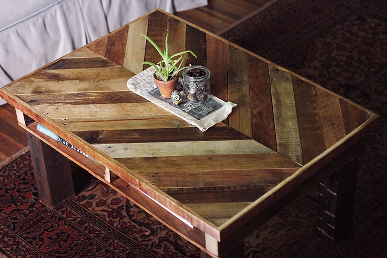 Pallet wood coffee table with a chevron pattern top in mixed wood tones, holding a small potted succulent on a rug