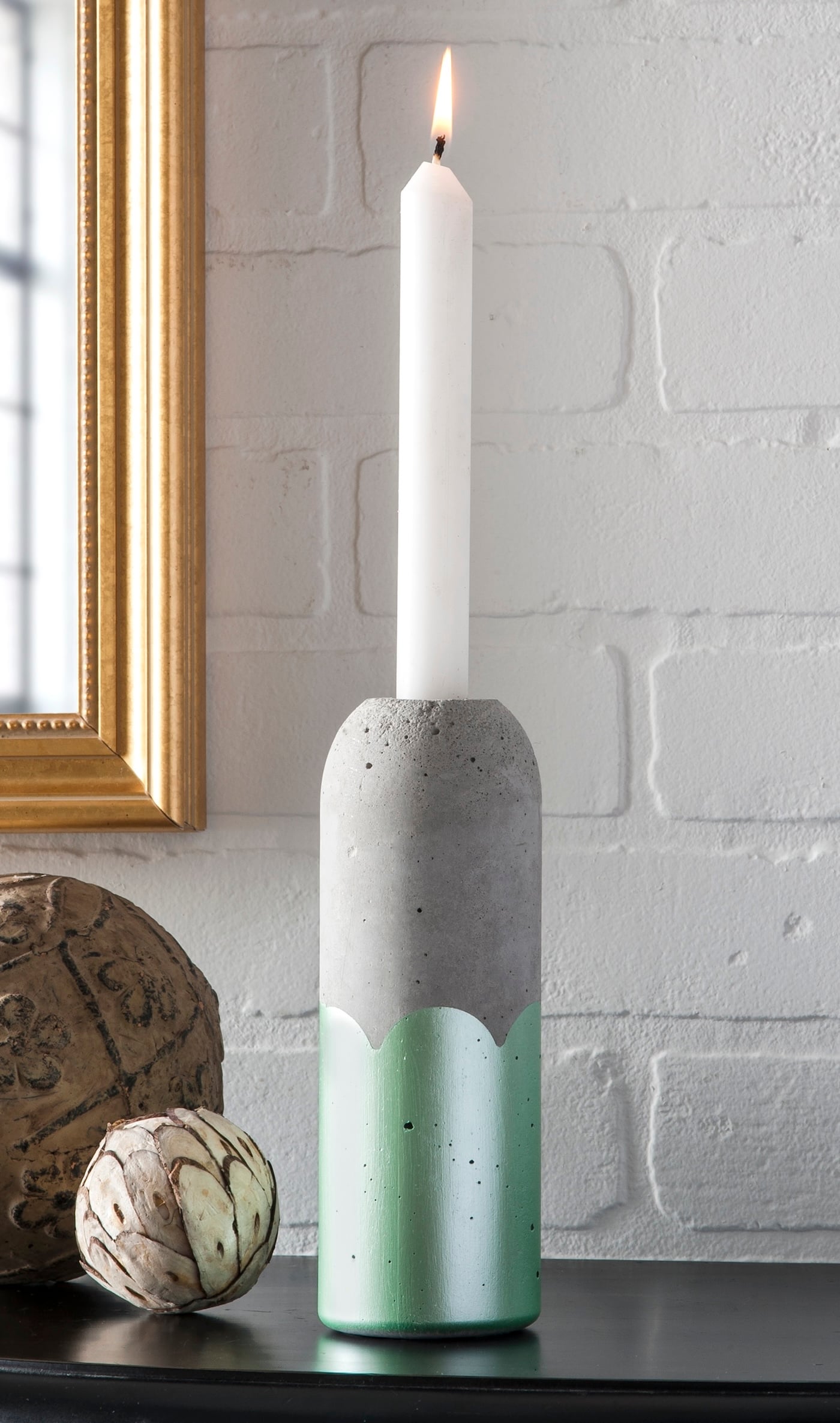 Concrete Bottle Candle Holders | Recycled Mold DIY Tall concrete taper candle holder cast in a plastic bottle, its base dipped in mint green paint, on a shelf by a gold mirror
