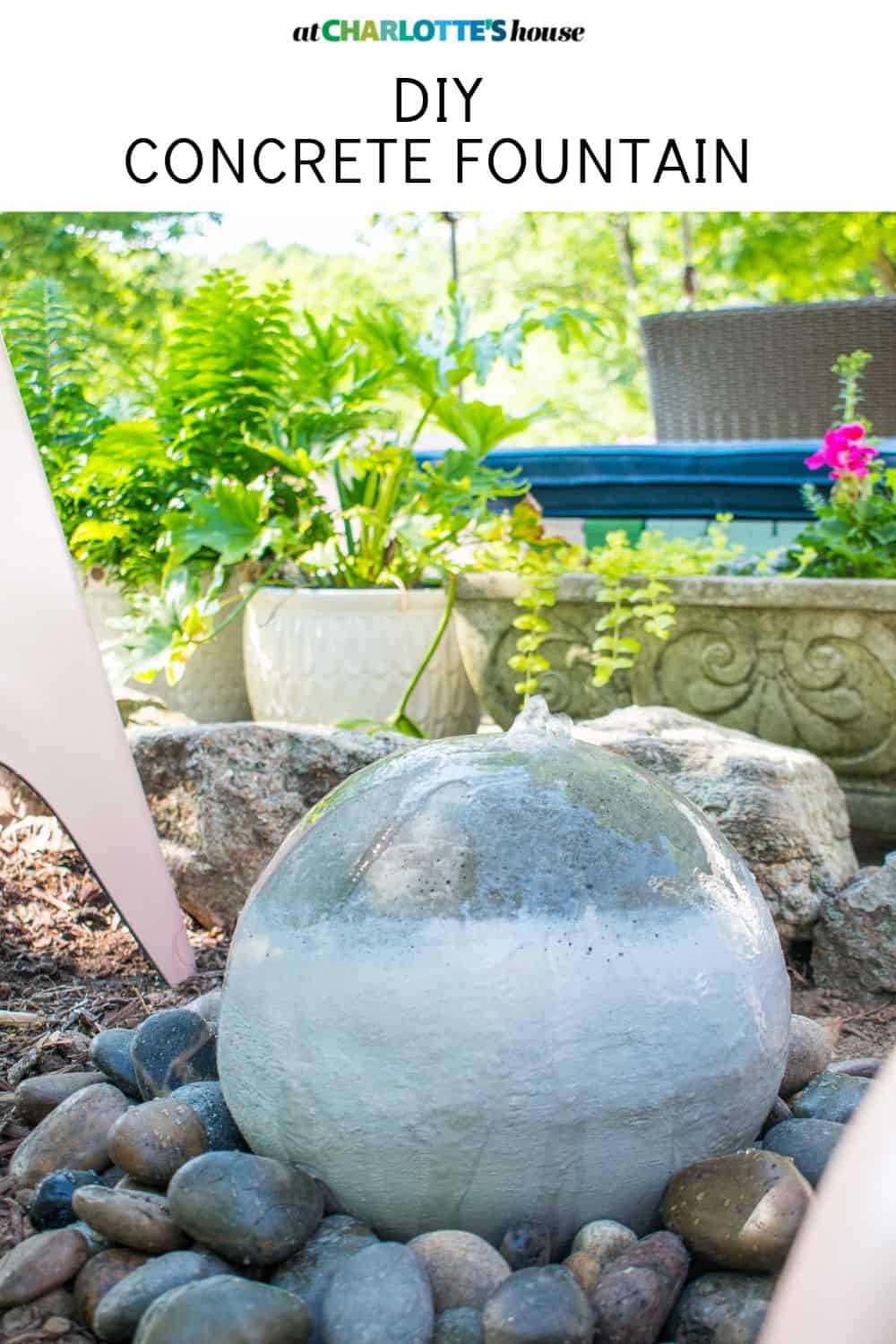 DIY Concrete Fountain Orb | Garden Fountain Under $100 Gray concrete sphere fountain with water flowing over the top, set in a bed of smooth river rocks in a green garden