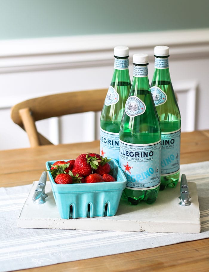 Concrete Tray with Dock Cleats | Coastal Serving Tray White concrete serving tray with metal dock cleat handles holding a basket of strawberries and three green water bottles