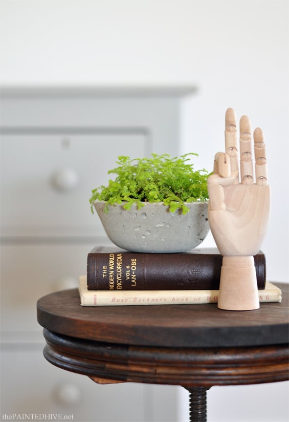 Concrete Vessel Planters | Small Bowl Planter DIY Small rough gray concrete bowl planter with bright green ferns, on books beside a wooden hand on a round wood stool