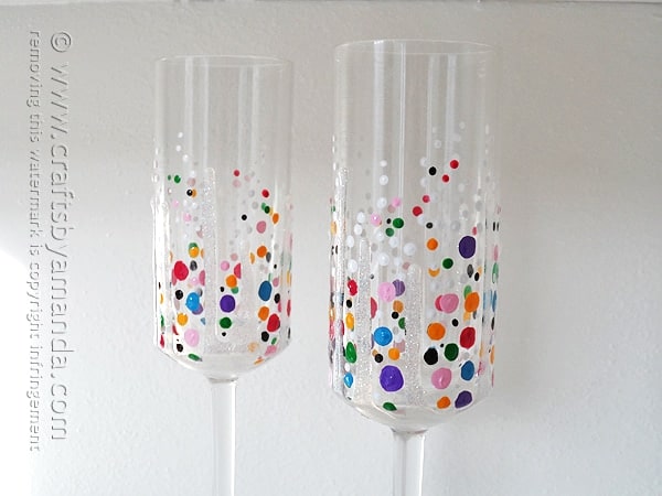 Two clear champagne flutes painted with rainbow confetti dots in pink, purple, blue, orange and green with glitter