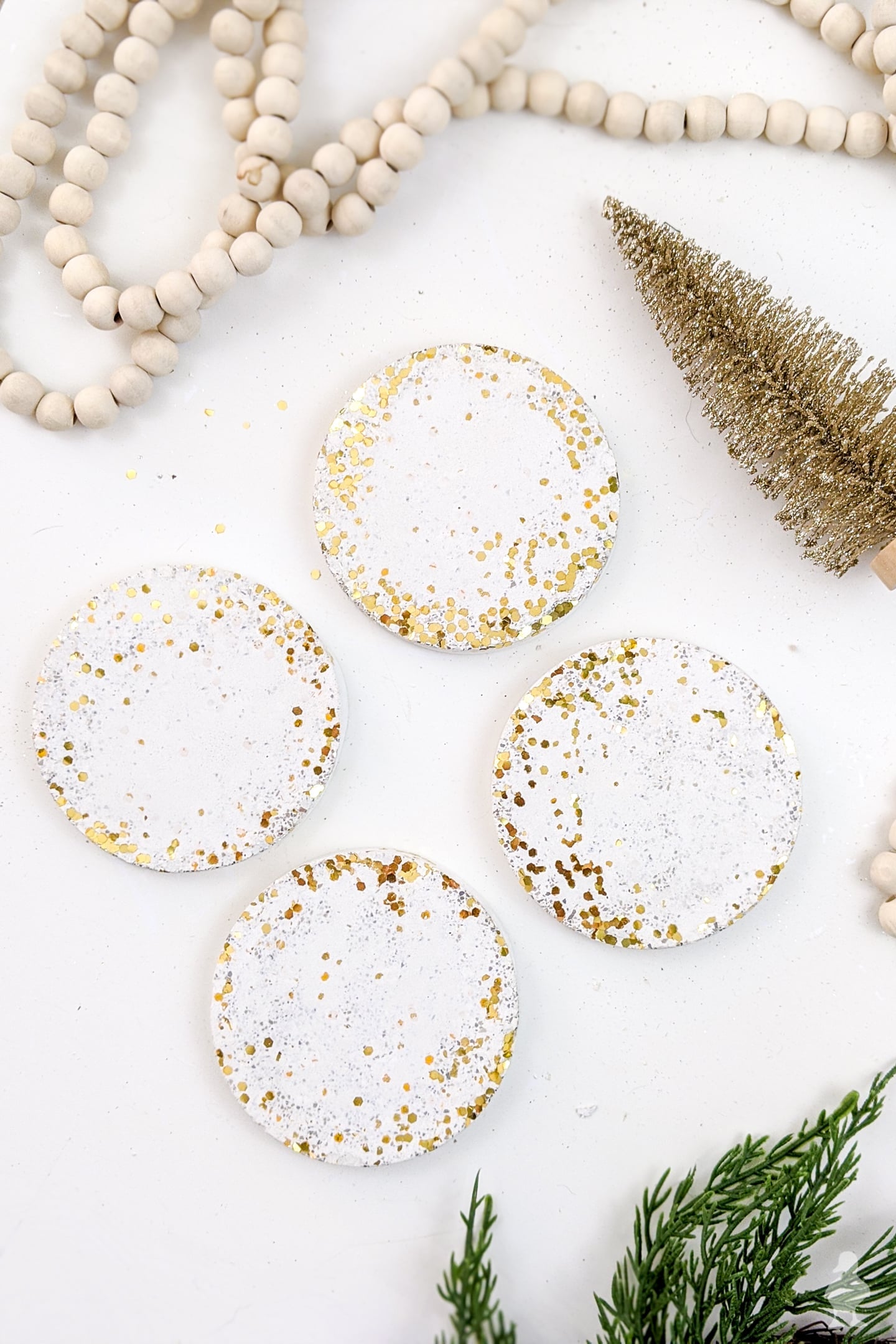 Confetti Concrete Coasters | Glitter Hostess Gift DIY Four round white concrete coasters with gold glitter swooped along one side, beside wood beads and a bottle brush tree