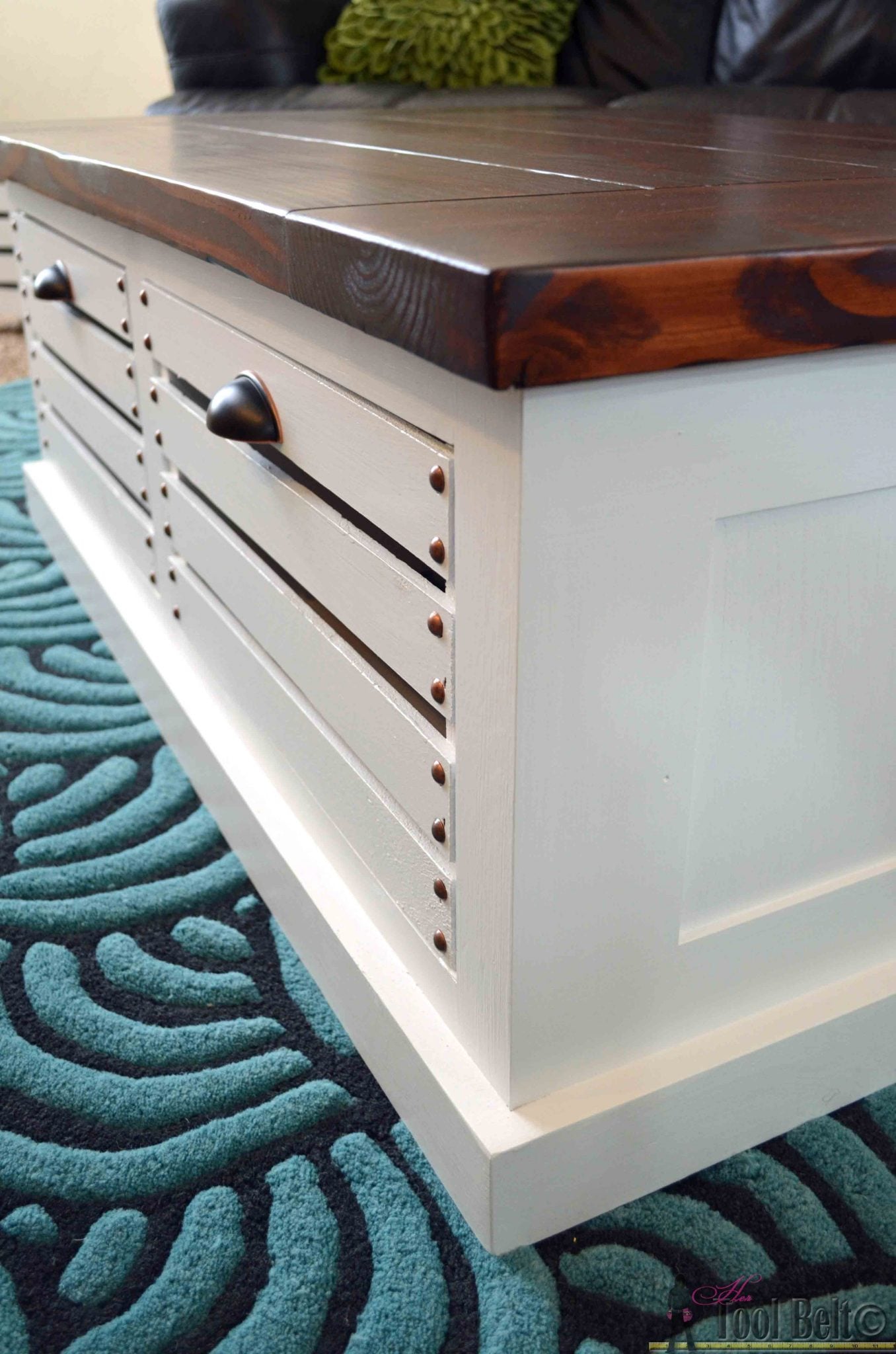 Close up of a white storage coffee table with slatted crate drawers and a dark stained wood top on a teal patterned rug