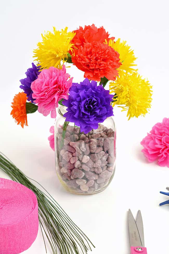 Crepe Paper Flowers | DIY Party Decorations Idea Bright crepe paper flowers in purple, pink, red, orange and yellow in a glass jar beside a pink streamer roll and wire