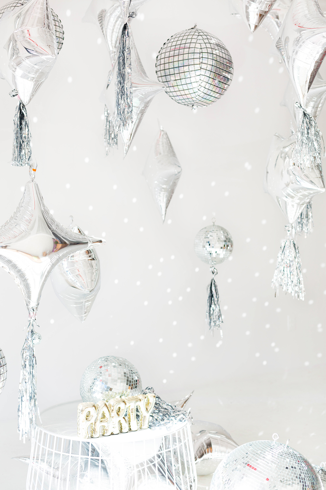 Silver balloons, disco balls and fringe tassels hanging at different heights as a New Year's Eve photo backdrop