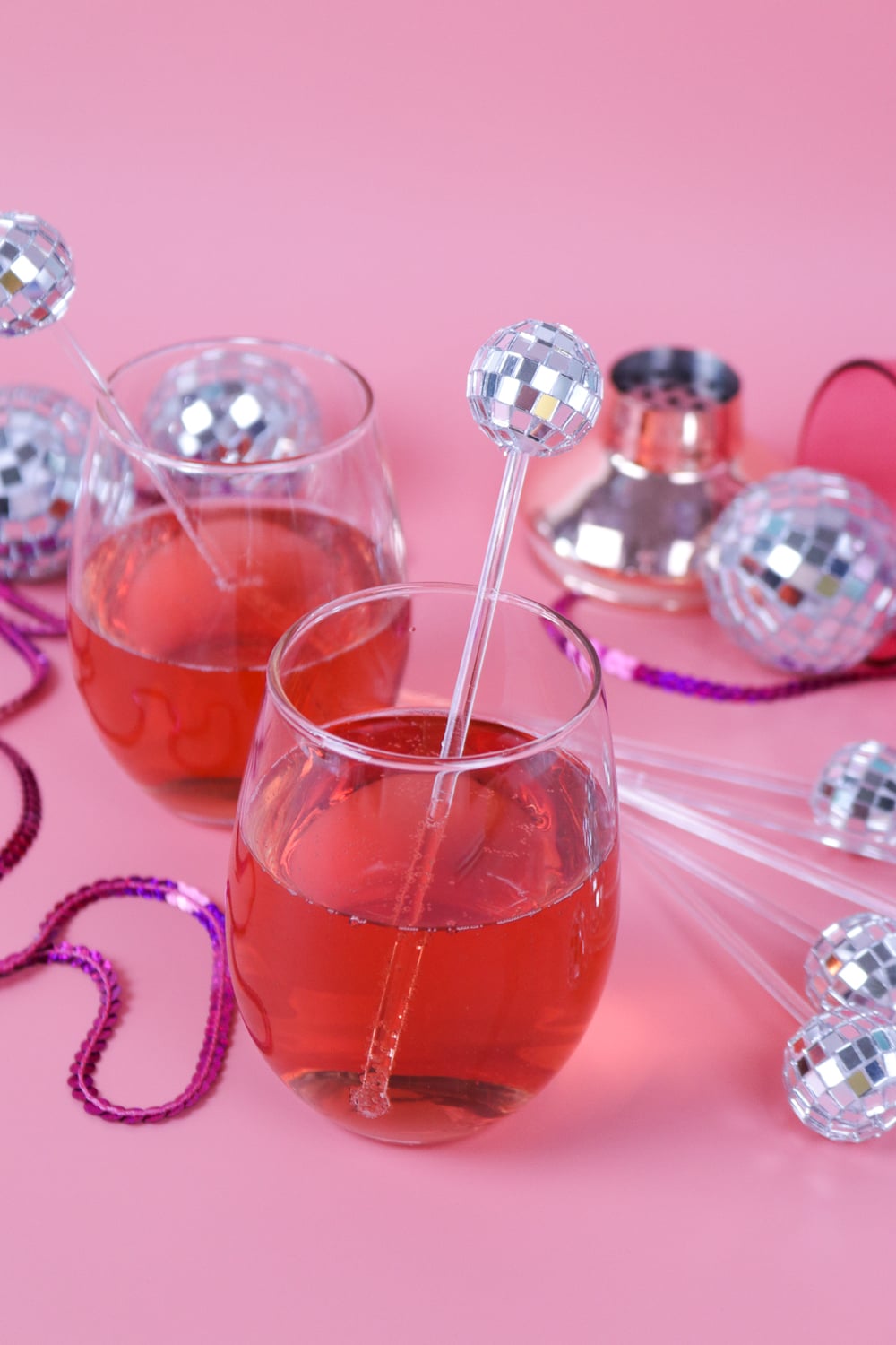 Disco Ball Drink Stirrers | DIY Party Decorations Idea Pink drinks in stemless glasses with mini disco ball drink stirrers on a pink table scattered with disco balls