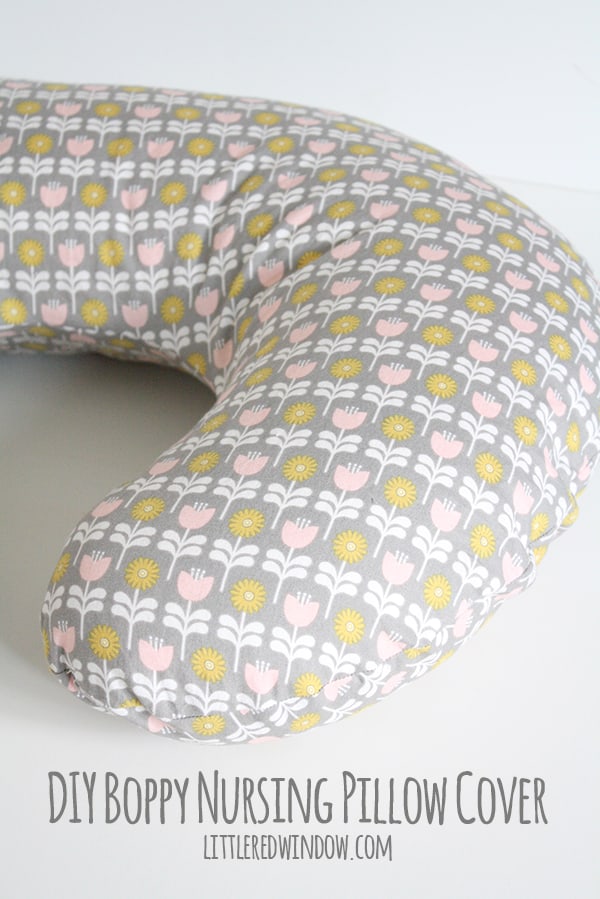 Nursing pillow cover in gray fabric printed with pink tulips and yellow flowers on a curved pillow against a white background