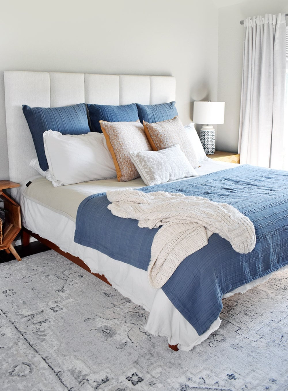 Cream channel tufted DIY headboard on a bed dressed with blue and white bedding, layered pillows and a cream knit throw