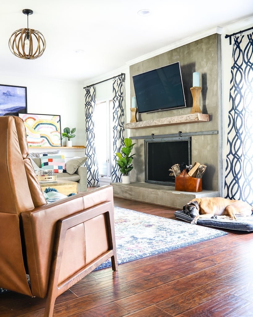 DIY Concrete Fireplace | Under $100 Makeover Living room with a smooth gray concrete fireplace wall, a TV above, a wood mantel, leather chairs and a sleeping dog