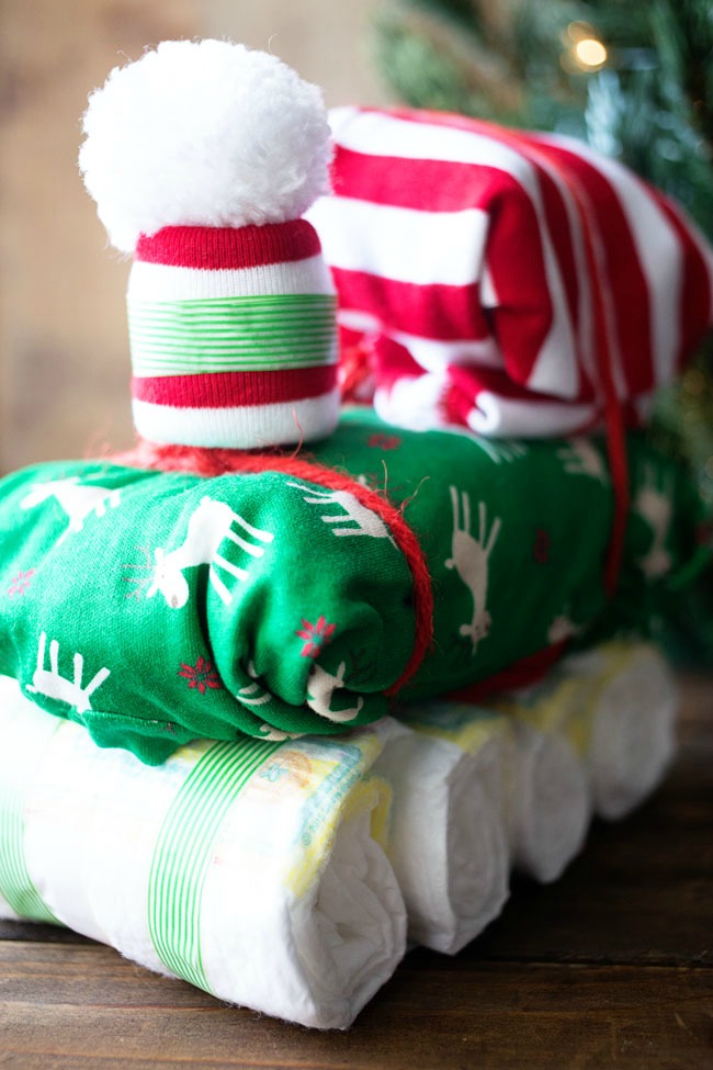 Diaper train gift with rolled diaper wheels, green reindeer blanket and red striped cab and a pom pom baby hat smokestack