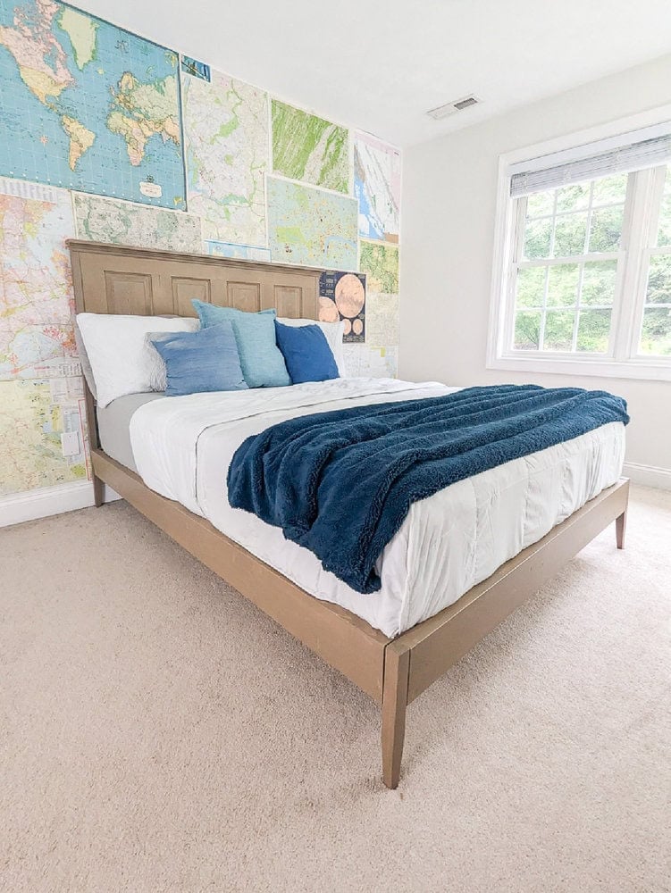 Freestanding headboard made from an old paneled door with a matching wood bed frame against a map covered wall