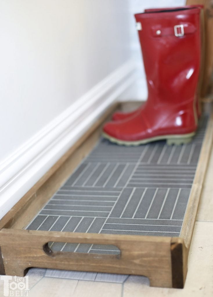 DIY Tile Boot Tray | Mosaic Entryway Mud Tray DIY tile boot tray, a stained wood frame with handles around gray parquet mosaic tile, holding red rain boots by a wall