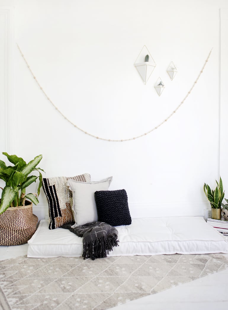DIY Tufted Daybed Cushion | Home Sewing Project White tufted floor daybed cushion with knit and striped pillows, gray throw and plants against a white wall with garland