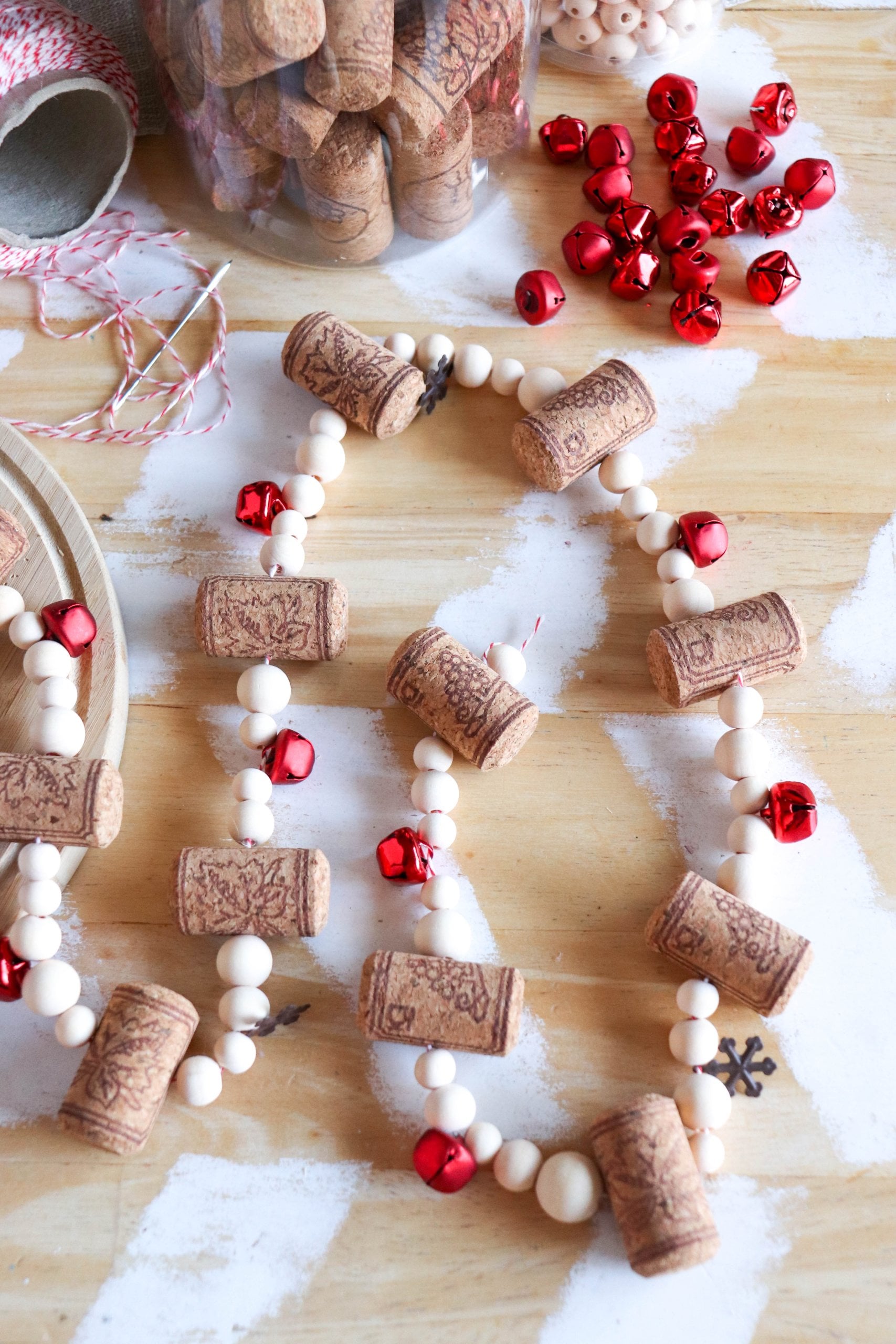 DIY wine cork garland of corks, natural wooden beads and red jingle bells on twine laid across a white painted table