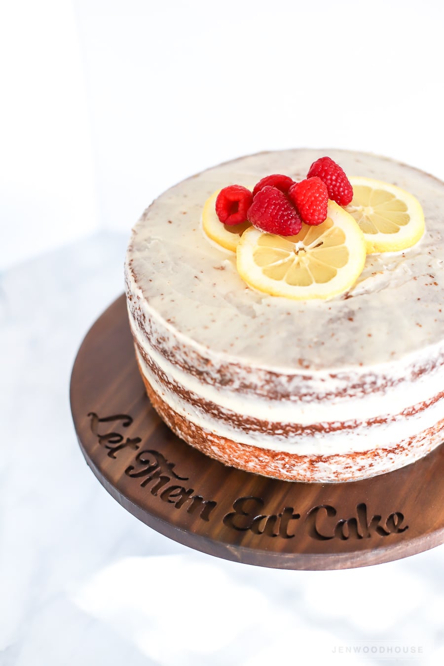 DIY Wood Cake Stand | DIY Party Decorations Idea Naked layer cake topped with raspberries and lemon slices on a dark wood cake stand carved with Let Them Eat Cake