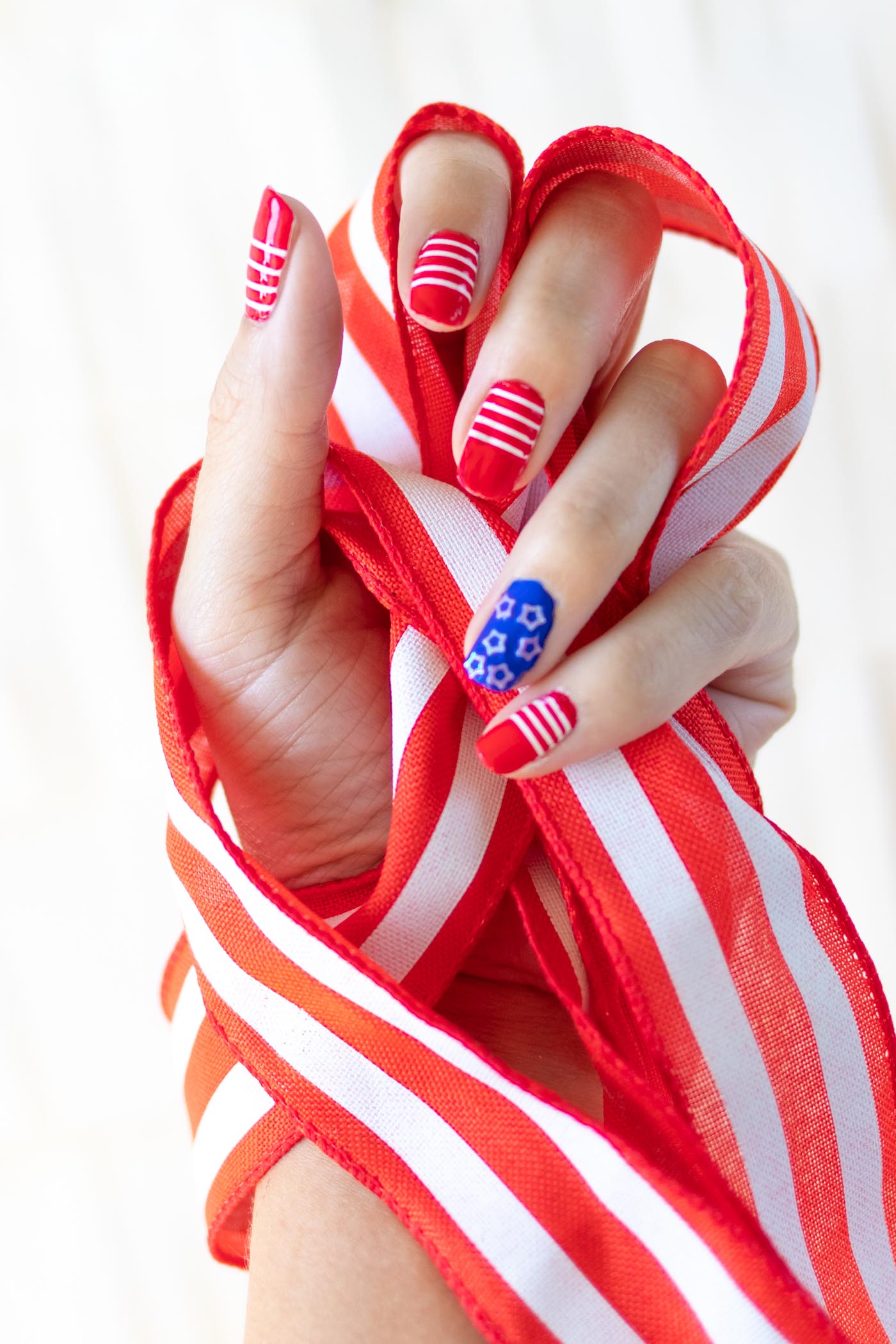 4th of July Stars and Stripes Nails | Quick Nail Art Idea Red and white striped nails with a blue star accent nail on a hand wrapped in red and white ribbon for the 4th of July