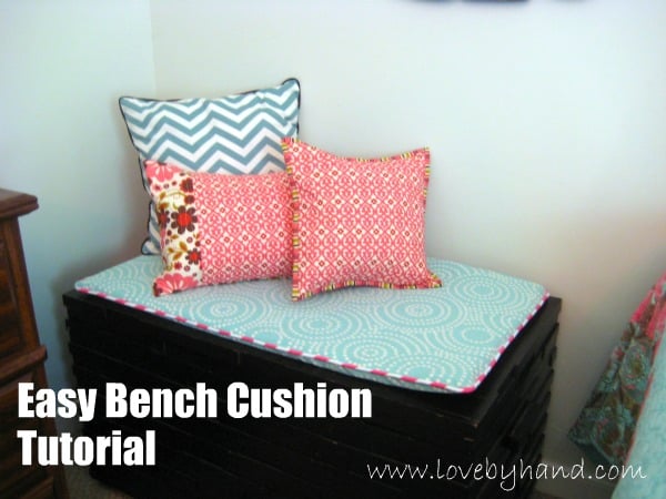 Easy Bench Cushion With Piping and a Zipper | Home Sewing Project Aqua patterned bench cushion with pink piping on a black storage trunk, topped with a chevron pillow and two pink pillows