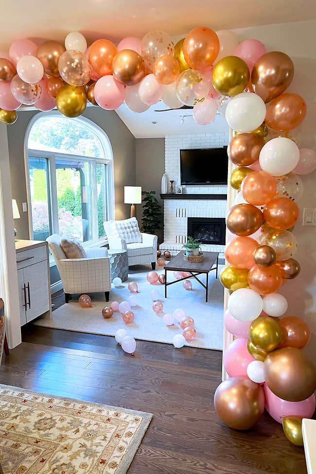 Pink, white, rose gold and gold balloon garland arching around a doorway into a living room with balloons on the floor