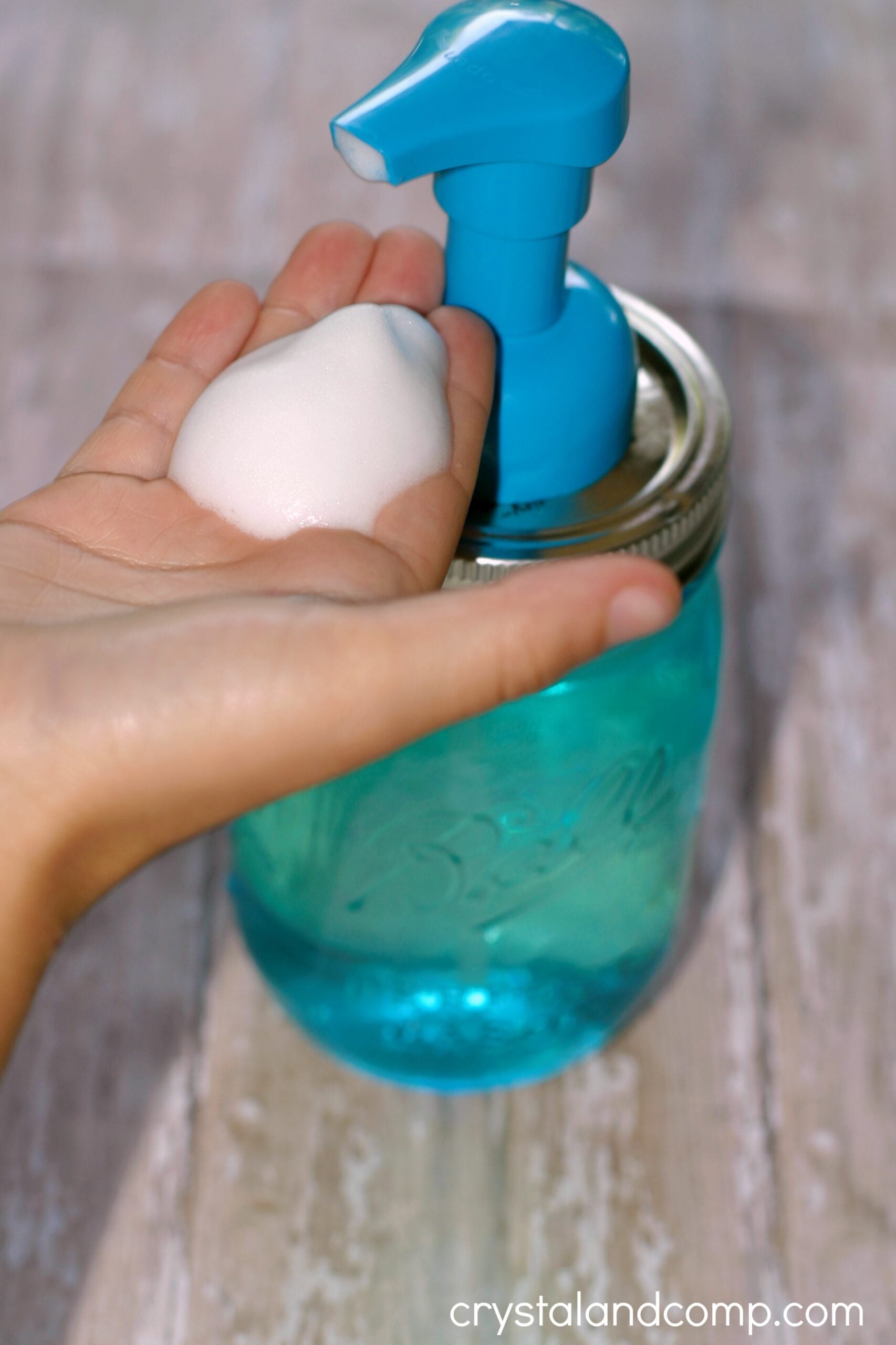 Blue Ball mason jar fitted with a turquoise foaming pump while a hand below holds a dome of fresh white soap foam