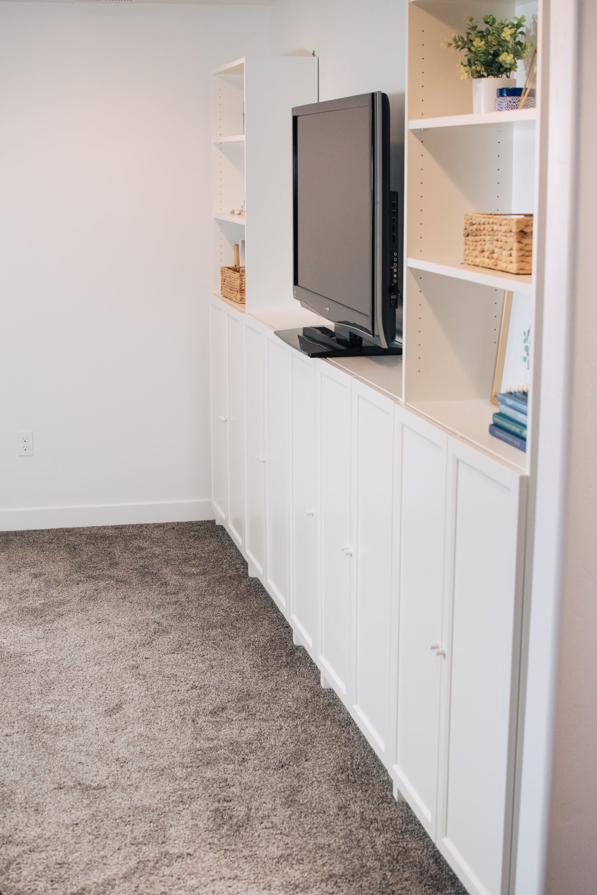 White IKEA Billy bookcases with Oxberg doors forming a TV wall with tall shelves and low cabinets in a carpeted basement