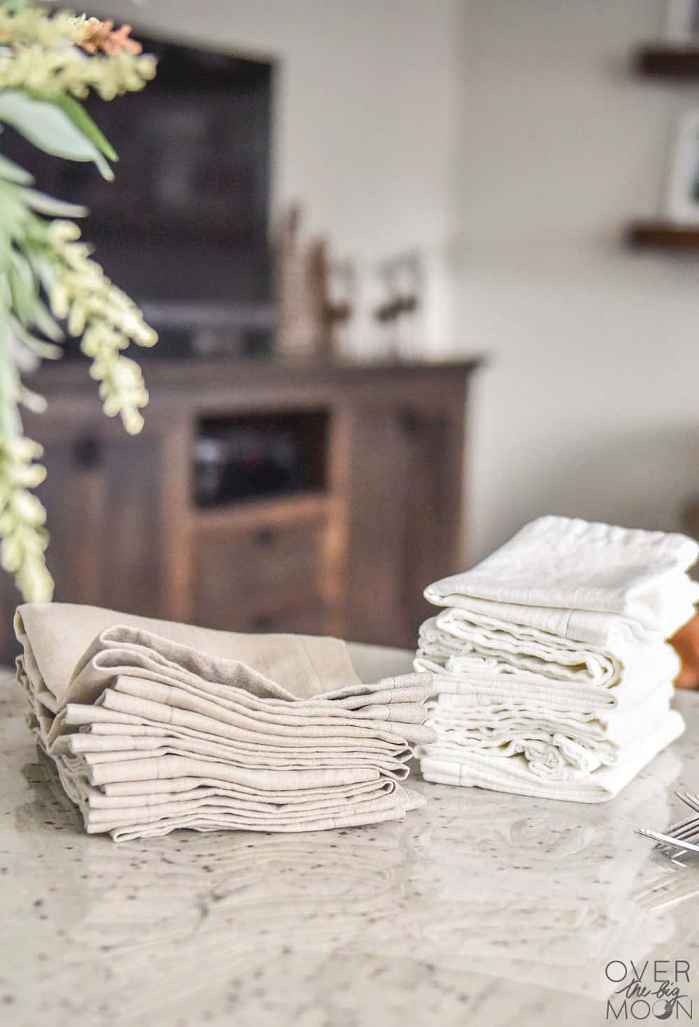 Easy Linen Dinner Napkins | Beginner Sewing Stacks of natural linen and white handmade cloth dinner napkins folded on a marble kitchen counter with greenery