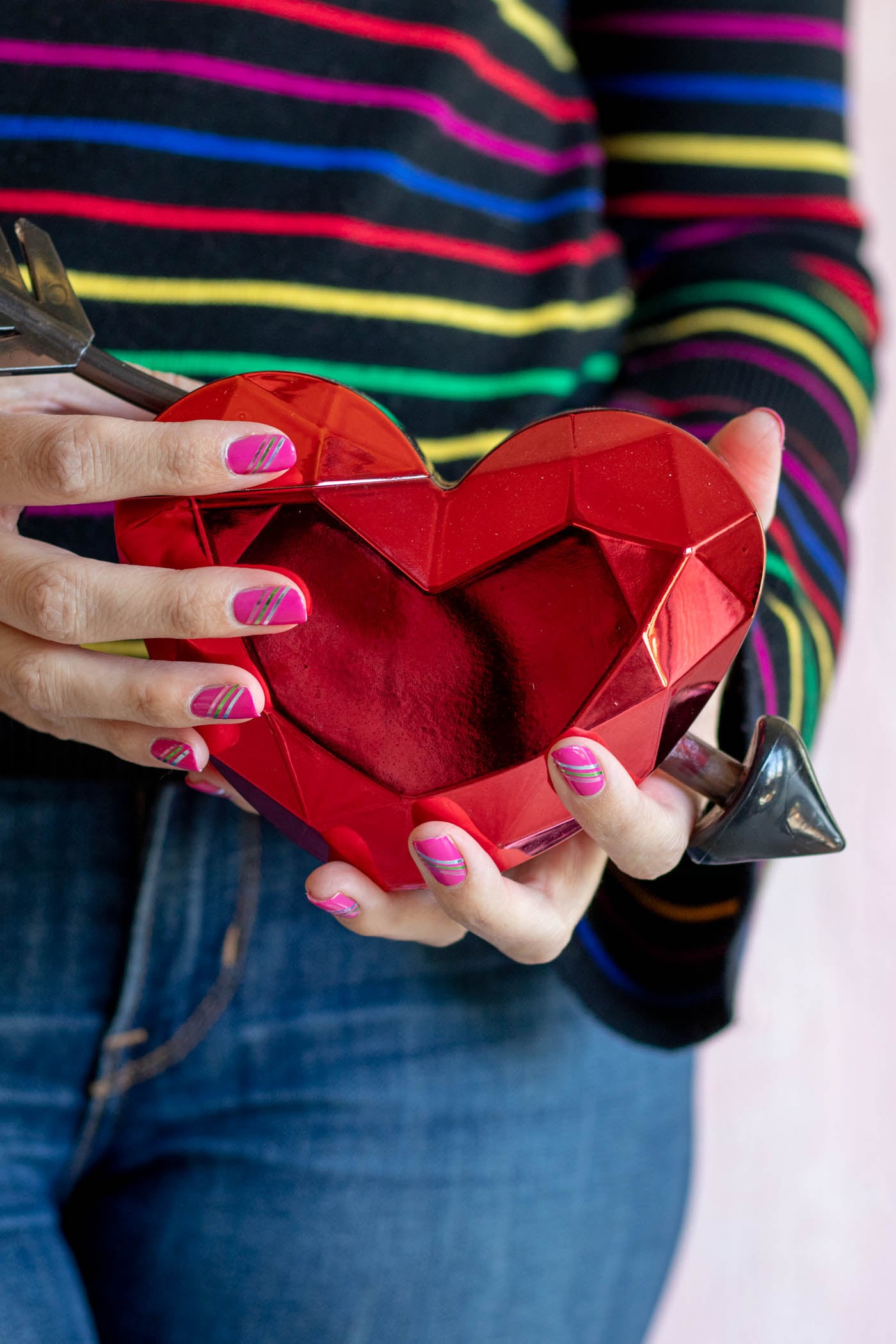 Easy Metallic Striped Nail Art | Quick Nail Art Idea Hot pink nails with thin diagonal gold, silver and rose metallic tape stripes on hands holding a shiny red faceted heart dish
