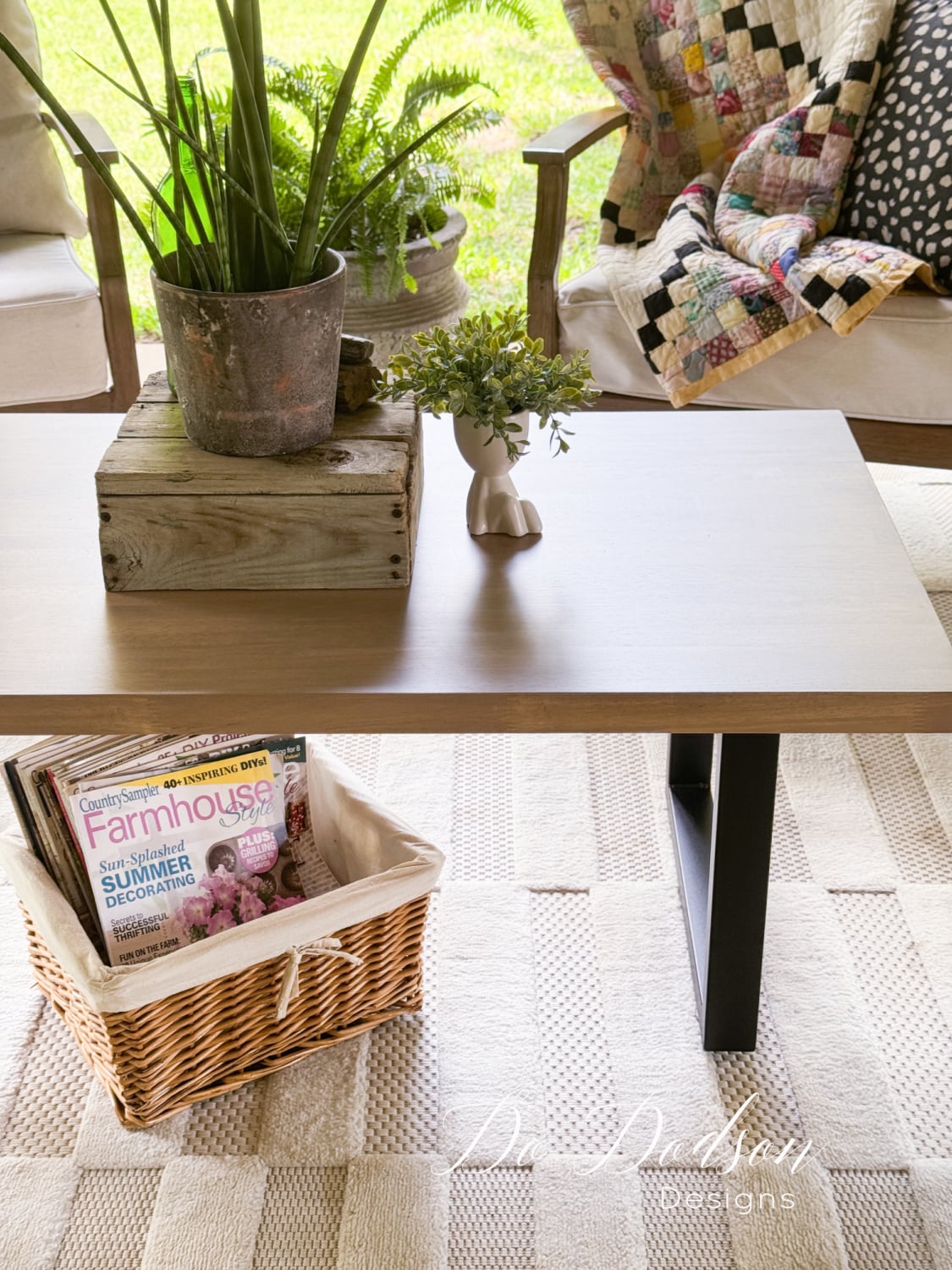 Outdoor coffee table with a warm brown wood top on black metal legs, a fern on a rustic crate and a wicker basket below