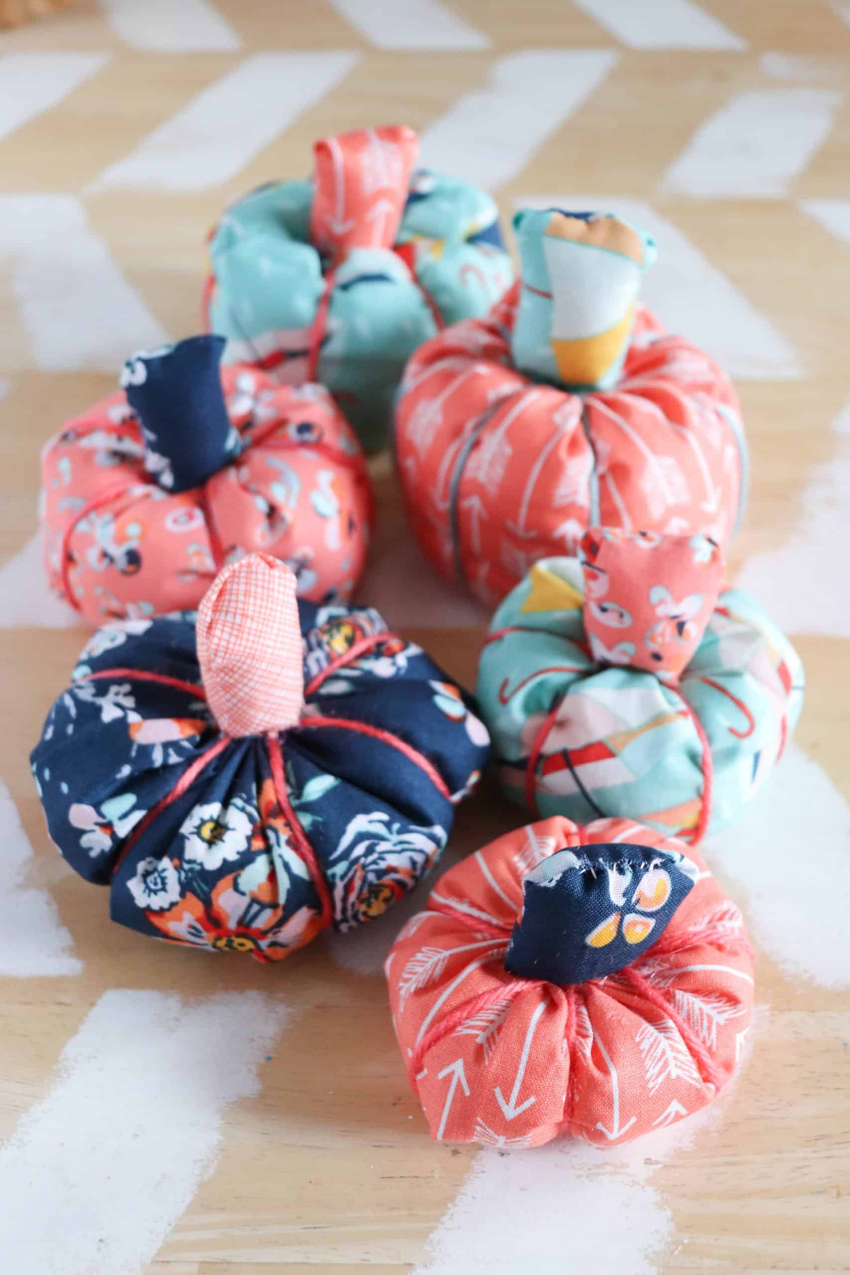 Easy Scrap Fabric Pumpkins | Home Sewing Project Six stuffed fabric pumpkins in coral, aqua and navy floral prints with fabric stems on a white painted wood tabletop