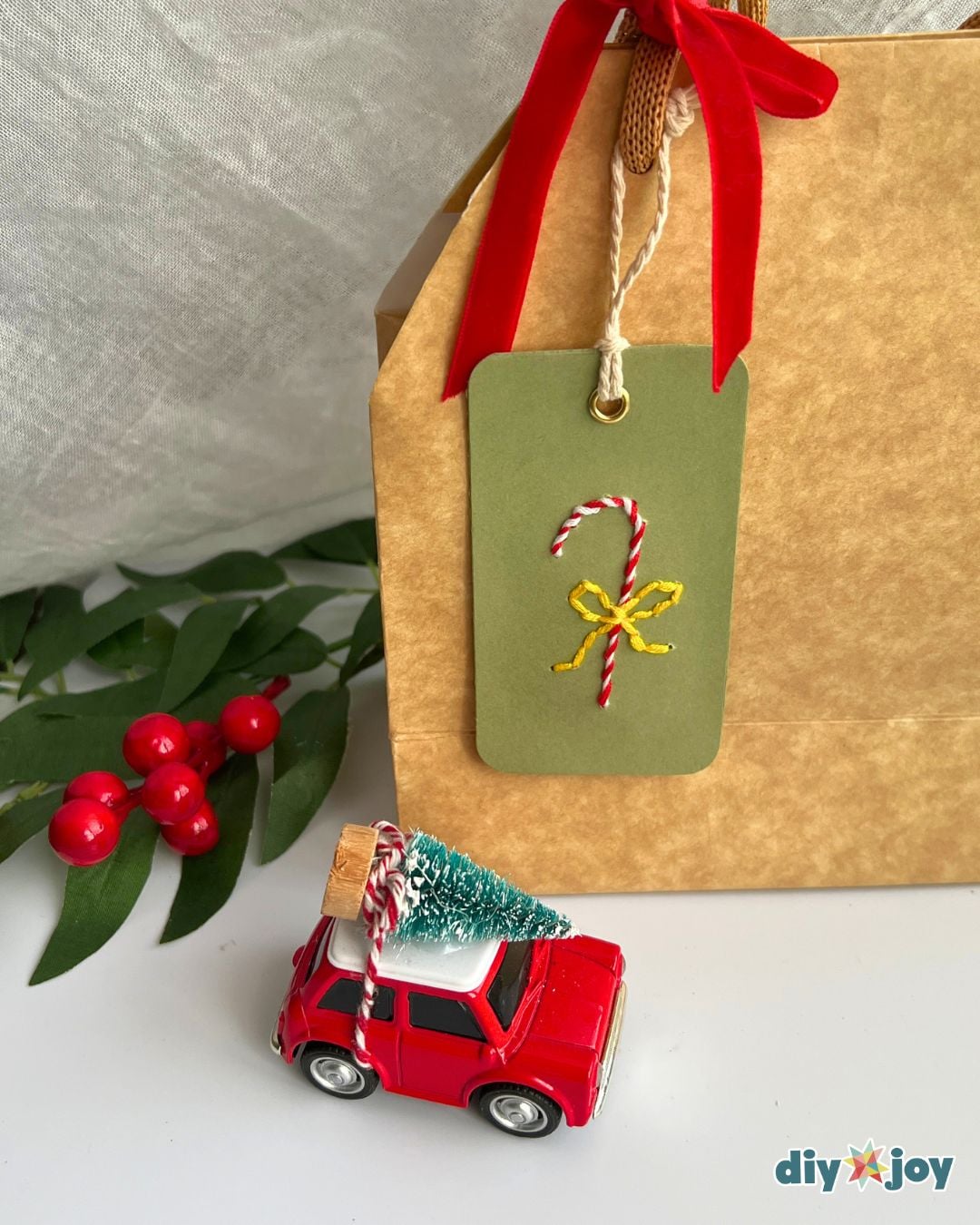 Handmade Christmas gift tag - embroidered candy cane tag hanging on a kraft gift bag with a red ribbon