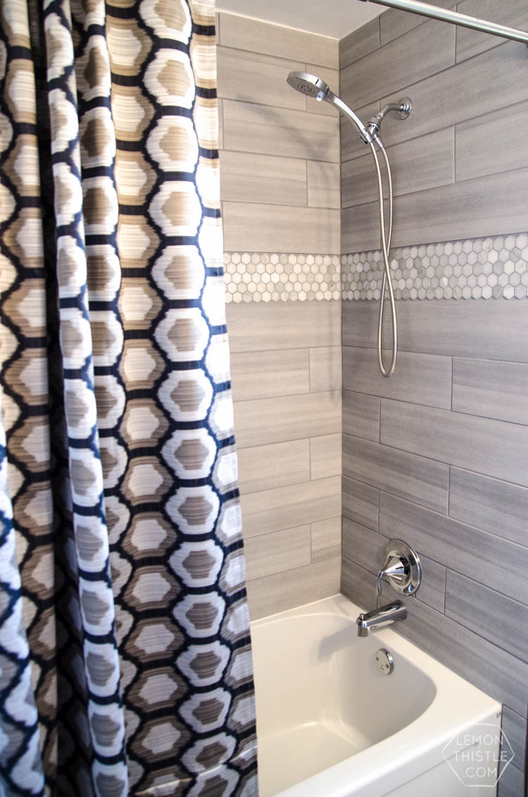 Extra long navy and gray hexagon print shower curtain hanging beside a gray tiled shower with a white tub