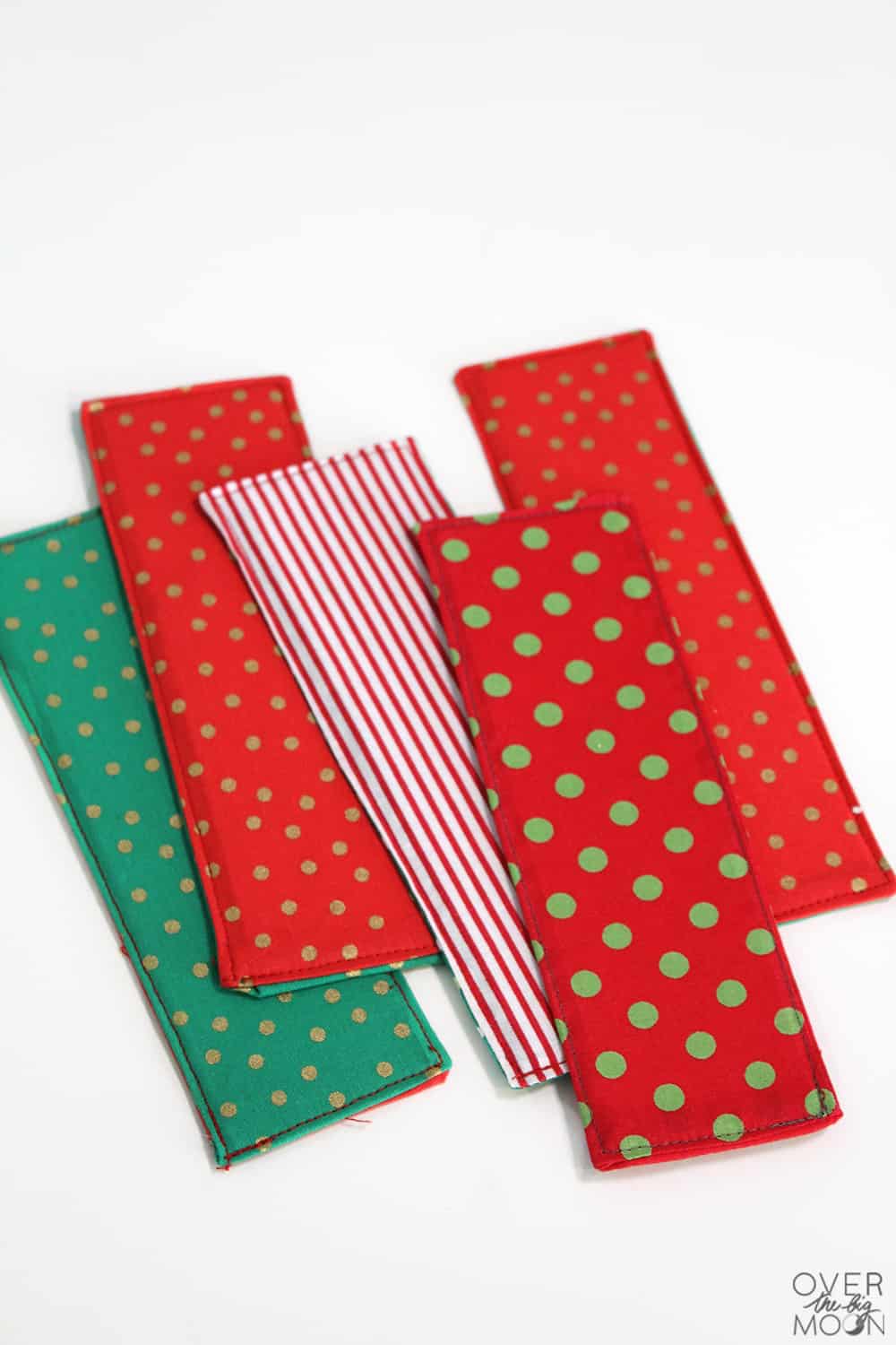 Easy Sew Christmas Fabric Bookmarks Five fabric bookmarks in red and green polka dot and red striped Christmas prints laid out on a white surface