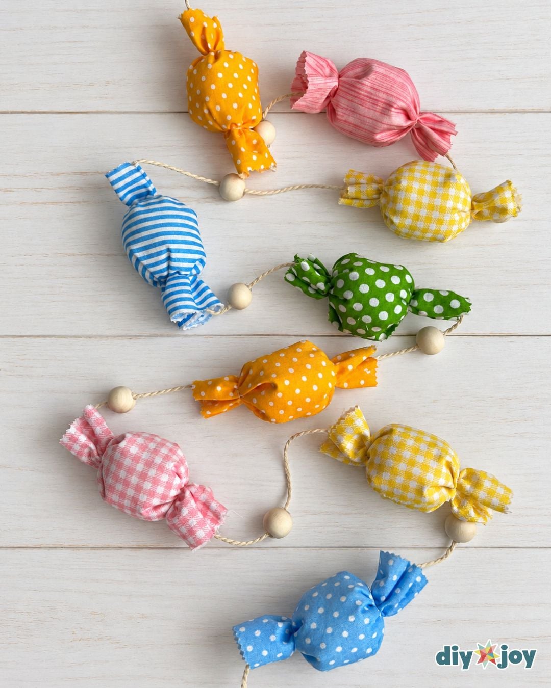 Fabric scrap candy garland of orange, pink, blue, green and yellow candies with wooden beads on white wood