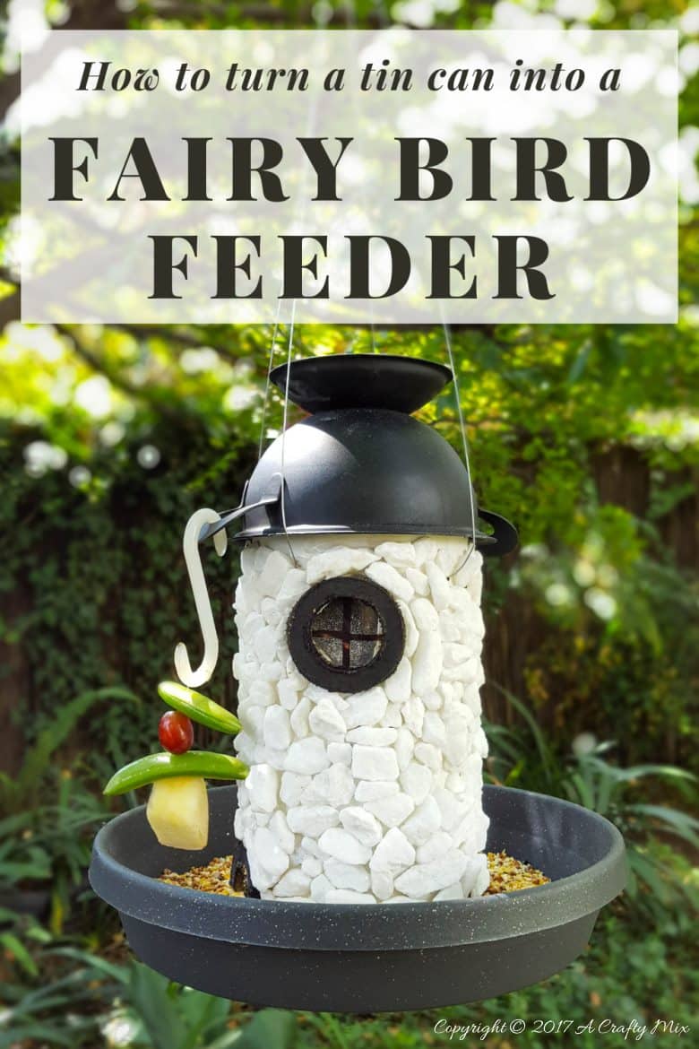 Hanging tin can fairy lighthouse bird feeder with a domed metal roof, small stones and a seed tray around the base