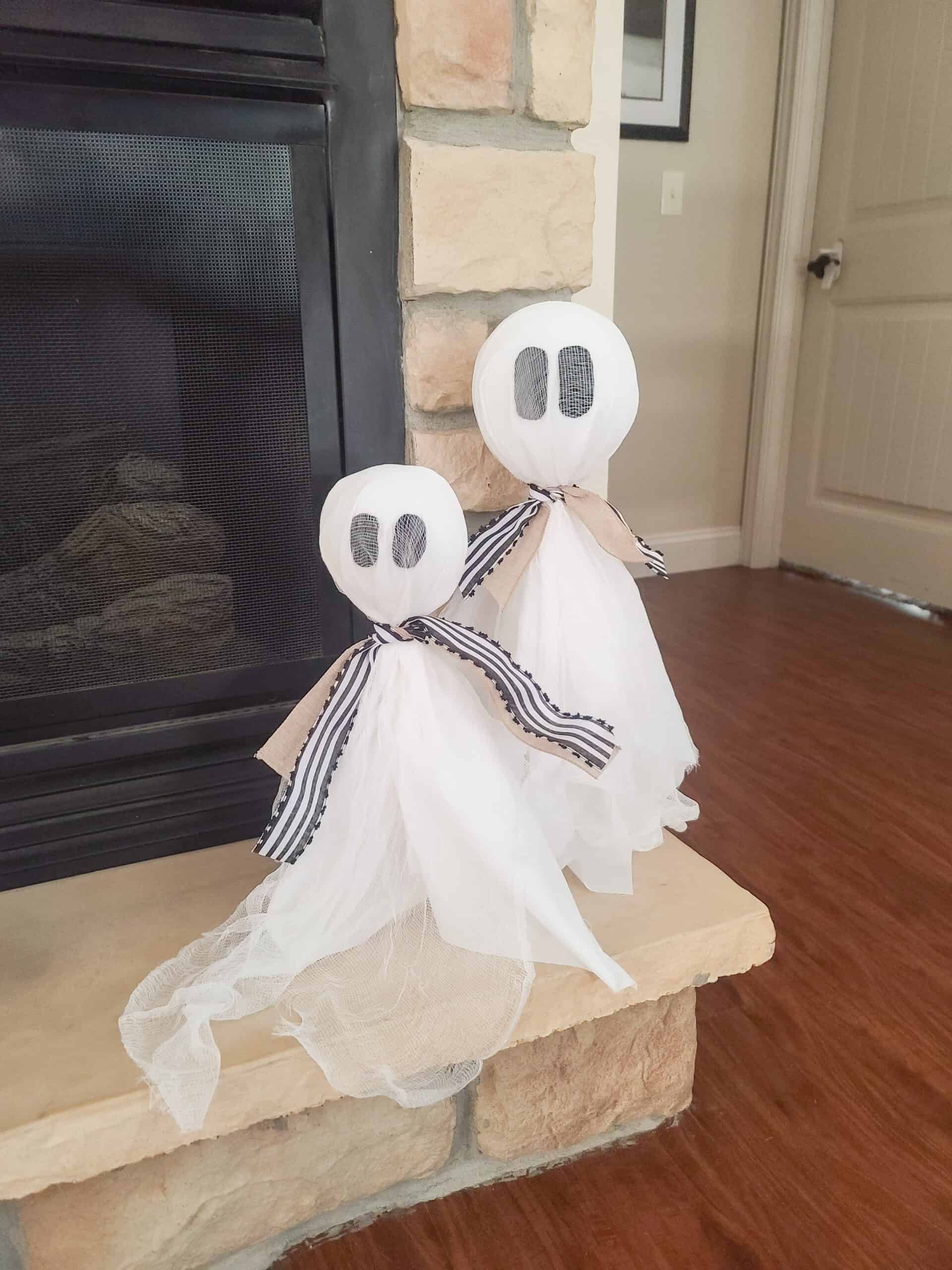 Farmhouse ghost topiary pair, cheesecloth ghosts with black felt eyes and striped bows on a stone hearth