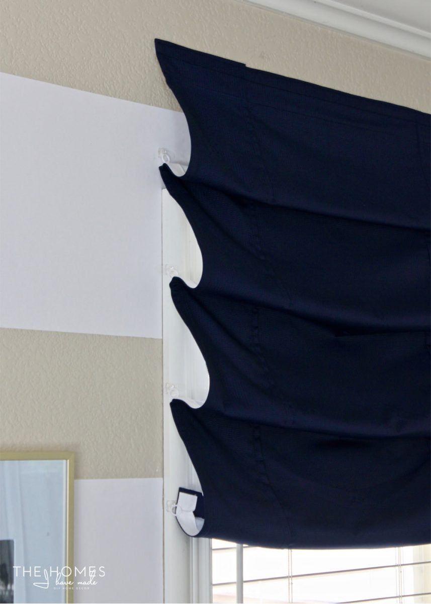 Faux Roman Shade | Home Sewing Project Navy faux roman shade with soft scalloped folds hung on a window beside a white and tan striped wall