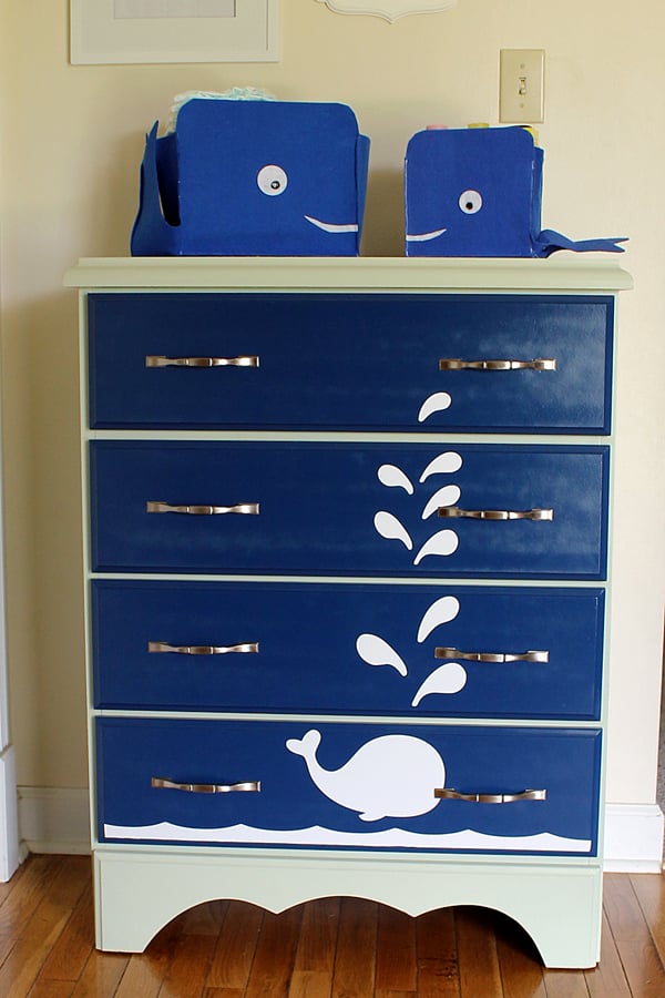 Navy painted dresser with white whale and water spout decals and two blue felt whale storage baskets on top