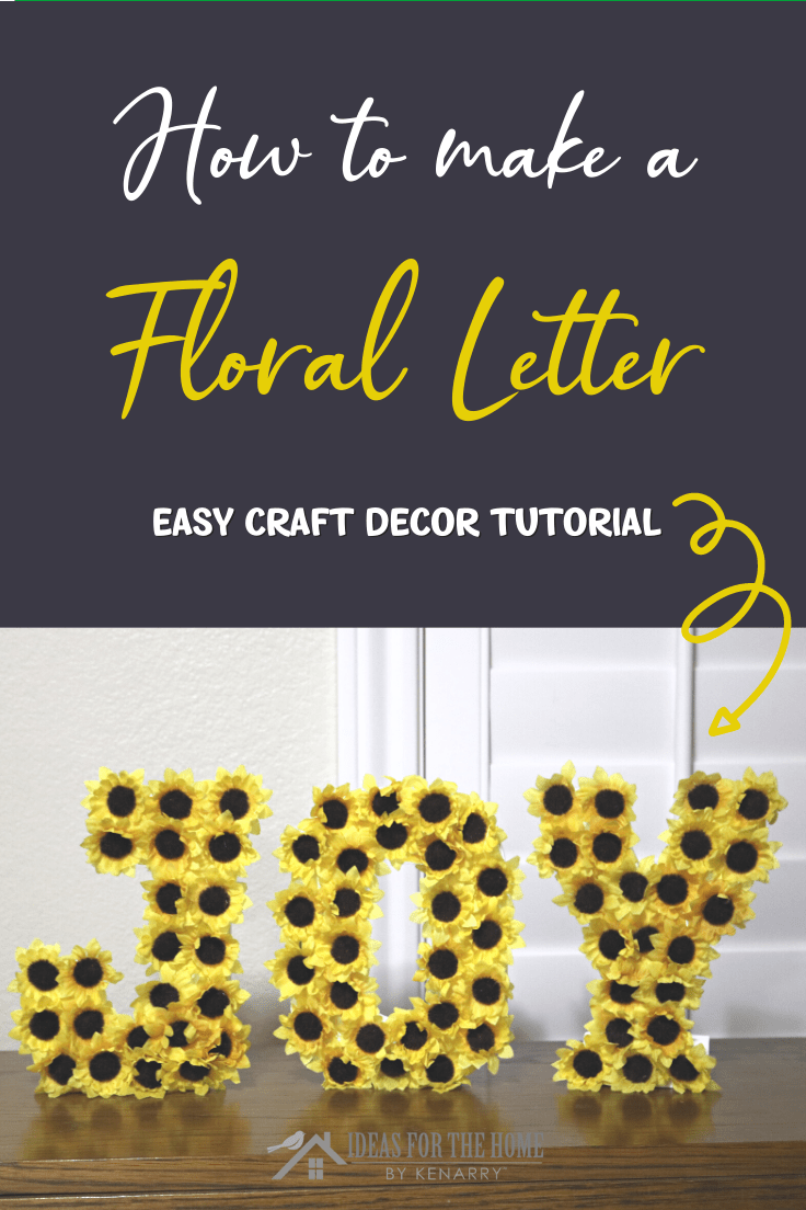 Wooden letters spelling JOY covered in yellow paper sunflowers with black centers on a wood shelf, under a title