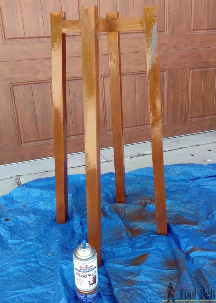 DIY flower pot stand, a tall four legged wood stand holding a basket of purple trailing petunias beside concrete porch steps