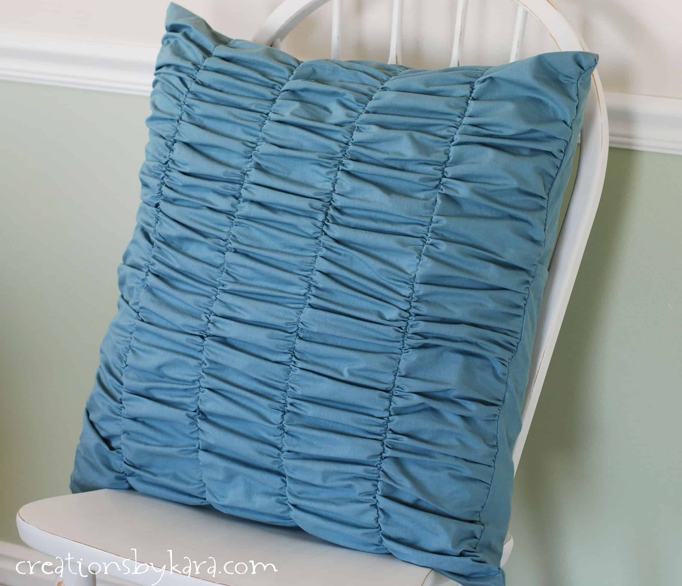 Gathered Decorative Pillow | Home Sewing Project Teal blue gathered ruched decorative pillow with rows of soft ripples leaning against a white wooden chair back